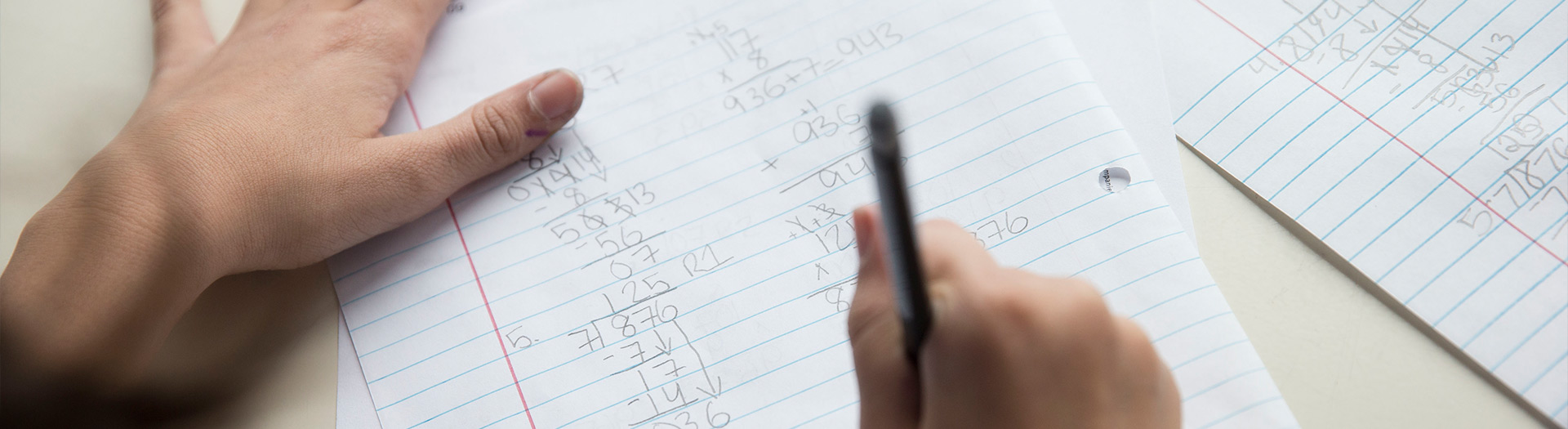 Hand with pencil writing out math equations.