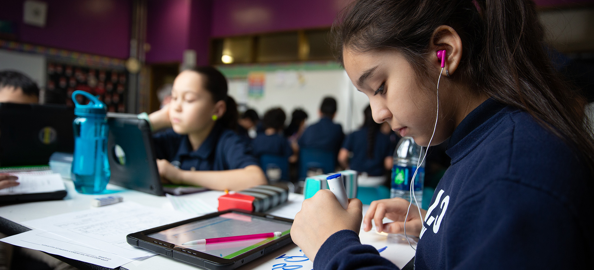学生们在教室的桌子上独立学习。一个学生戴着耳机，用记号笔写字。