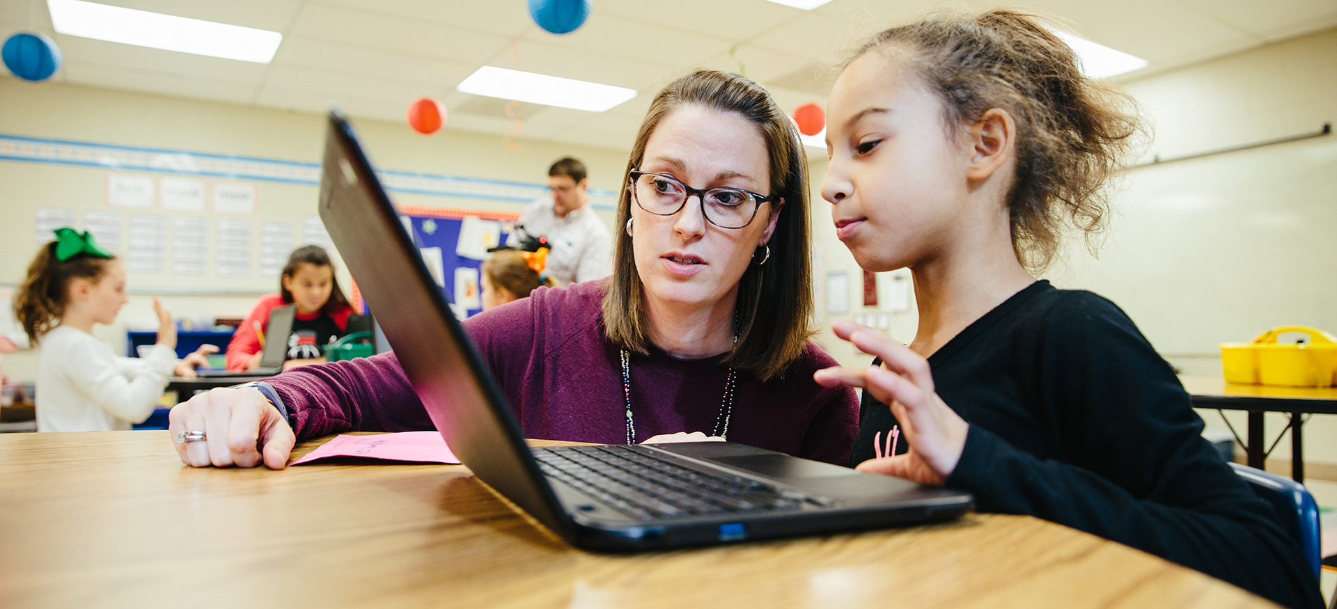 一位老师正在帮助一位在笔记本电脑上学习的学生。